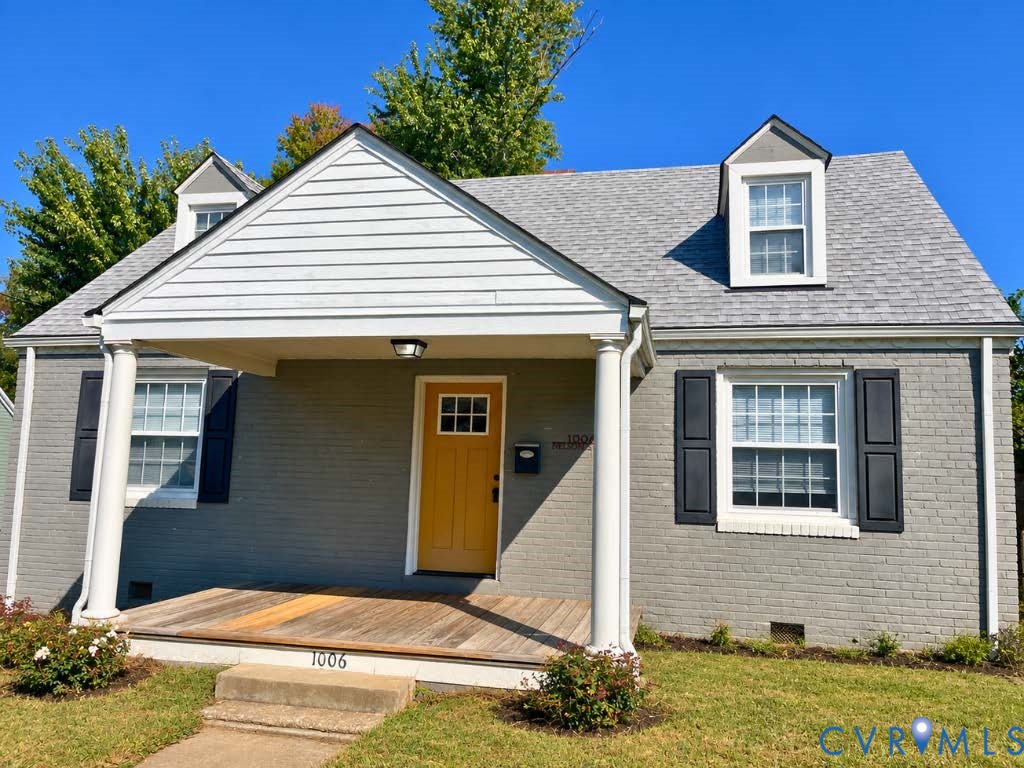 Painted brick exterior featuring a covered front porch with round columns, dormer windows, and a wood-plank porch deck Painted brick exterior featuring a covered front porch with round columns, dormer windows, and a wood-plank porch deck
