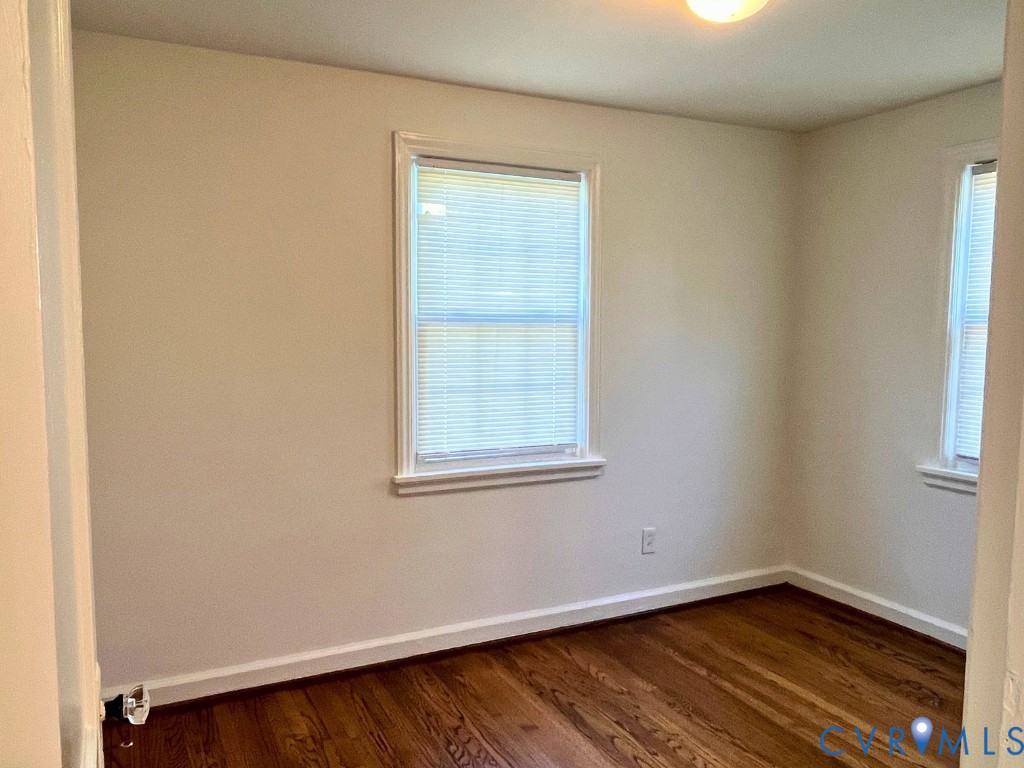 Room featuring wood-finish flooring, neutral-toned wall paint, and dual windows with window blinds Room featuring wood-finish flooring, neutral-toned wall paint, and dual windows with window blinds