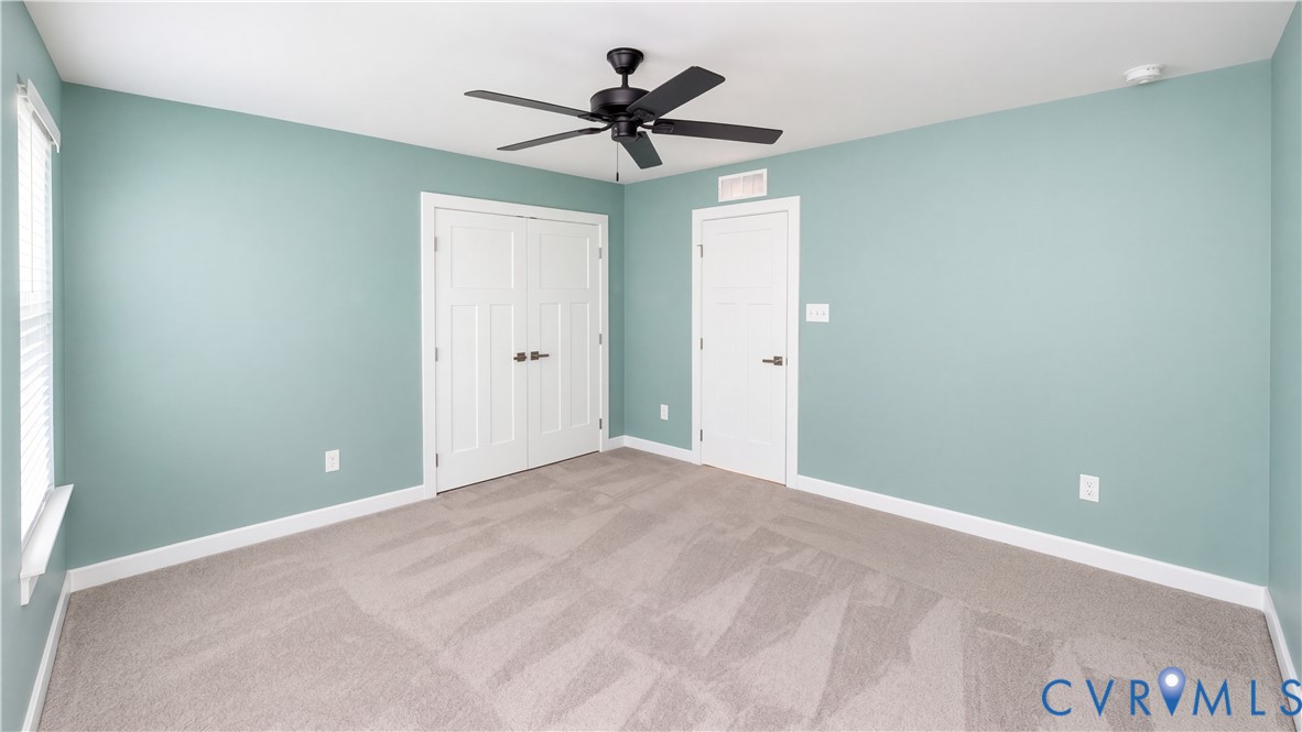 Room featuring carpeted flooring, neutral wall paint, a ceiling fan with matte black finish, double-panel closet doors, and a single-panel interior door