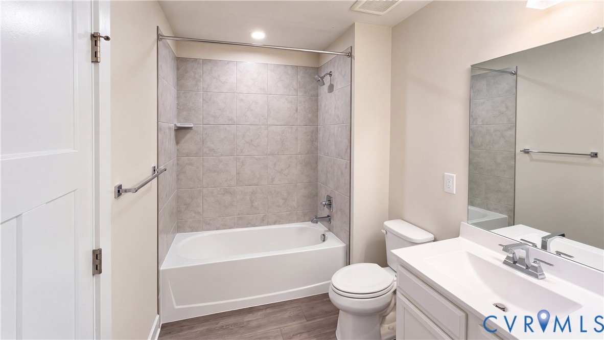 Bathroom featuring a vanity with an integrated sink, rectangular wall mirror, tub-shower combination with ceramic tile surround, and wood-finish flooring