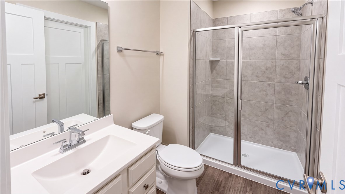 Bathroom featuring a vanity with a white countertop and integrated sink, a glass-enclosed shower with tile surround, wood-finish flooring, and a wall-mounted mirror