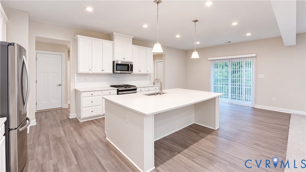 Kitchen featuring white shaker-style cabinetry, center island with stone-finish countertop, stainless steel appliances, recessed lighting, and wood-finish flooring Kitchen featuring white shaker-style cabinetry, center island with stone-finish countertop, stainless steel appliances, recessed lighting, and wood-finish flooring