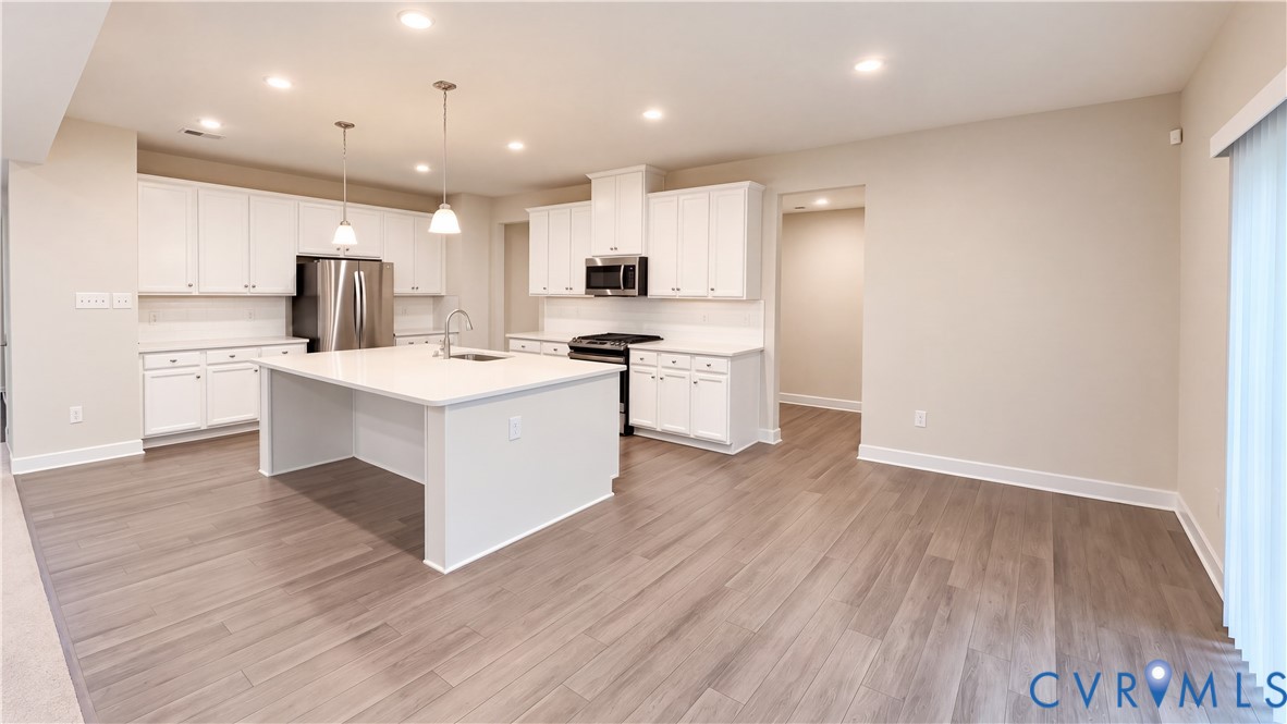 Kitchen featuring white cabinetry, a center island with a stone-surface countertop, wood-finish flooring, stainless steel appliances, and recessed ceiling lighting Kitchen featuring white cabinetry, a center island with a stone-surface countertop, wood-finish flooring, stainless steel appliances, and recessed ceiling lighting