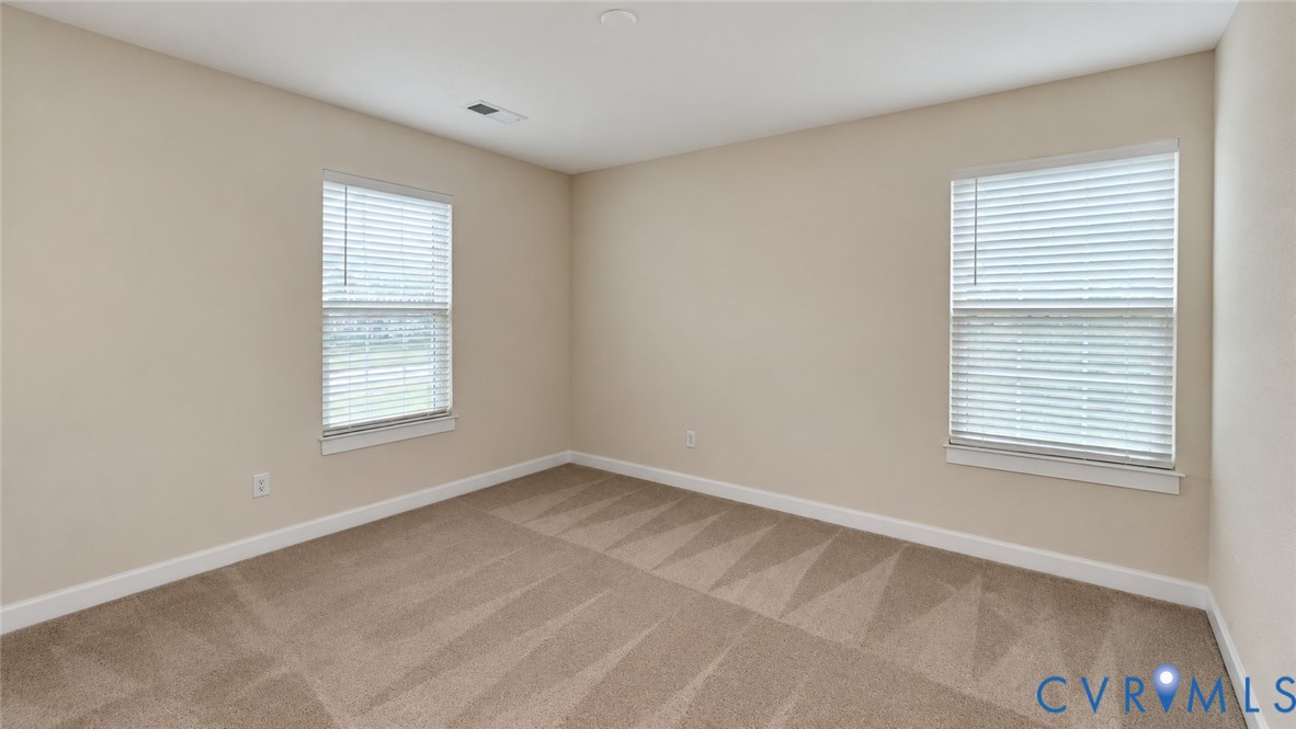 Neutral-toned interior space featuring wall-to-wall carpeting and two windows equipped with horizontal blinds
