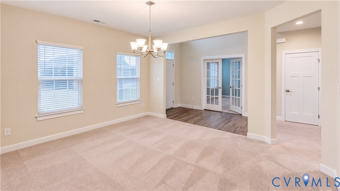 Neutral-toned interior featuring wall-to-wall carpeting, wood-finish flooring, multi-pane French doors, and a multi-light chandelier Neutral-toned interior featuring wall-to-wall carpeting, wood-finish flooring, multi-pane French doors, and a multi-light chandelier