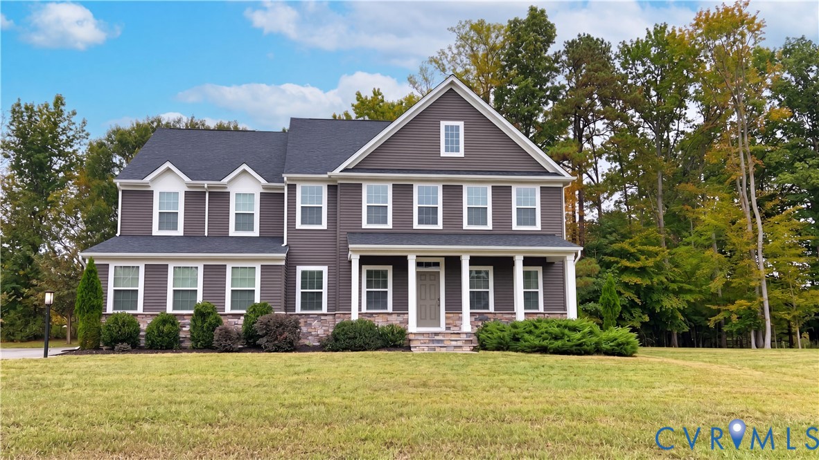 Two-story residence featuring a dark horizontal-siding exterior, stone-veneer foundation, gabled rooflines, dormer windows, and a covered front porch with white columns Two-story residence featuring a dark horizontal-siding exterior, stone-veneer foundation, gabled rooflines, dormer windows, and a covered front porch with white columns