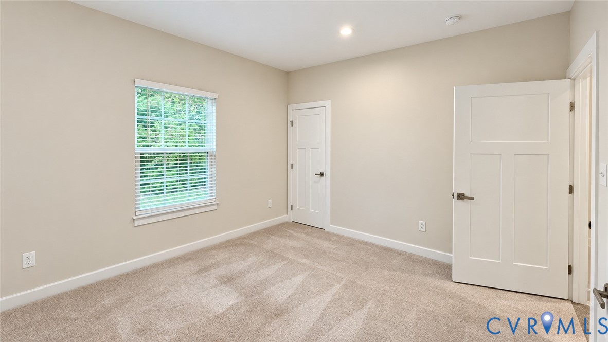 Neutral-toned room featuring wall-to-wall carpeting, recessed ceiling lighting, a single-hung window with horizontal blinds, and two-panel shaker-style interior doors with brushed nickel hardware