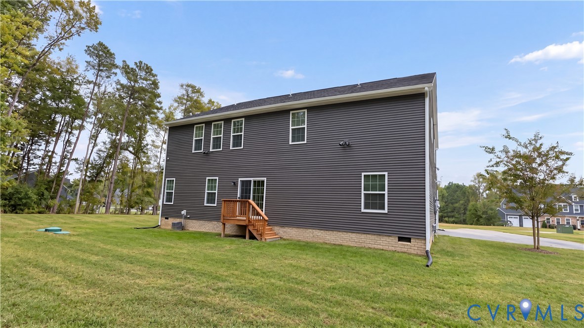 Dark-toned siding exterior featuring a stone-veneer foundation, rear wood deck, and expansive lawn with mature tree line