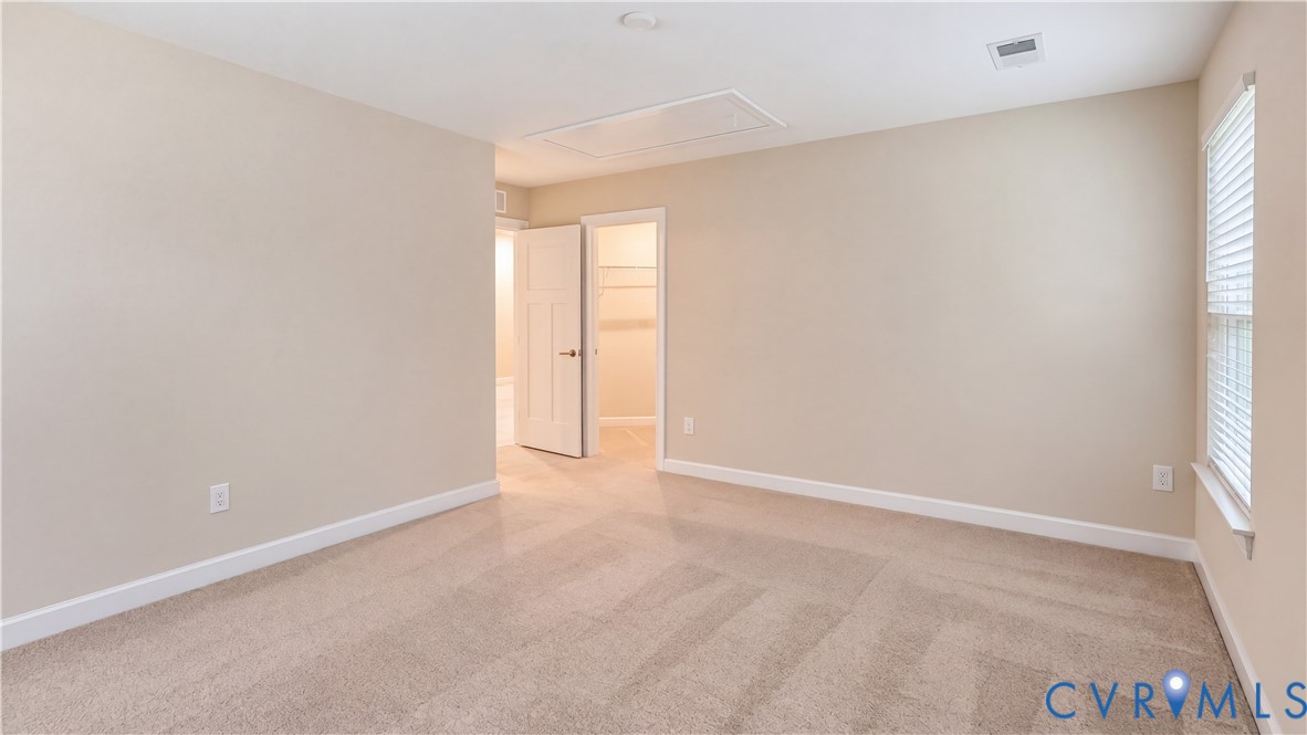 Neutral-toned room with plush wall-to-wall carpeting, window with slatted blinds, and an interior doorway providing access to a walk-in closet with built-in shelving