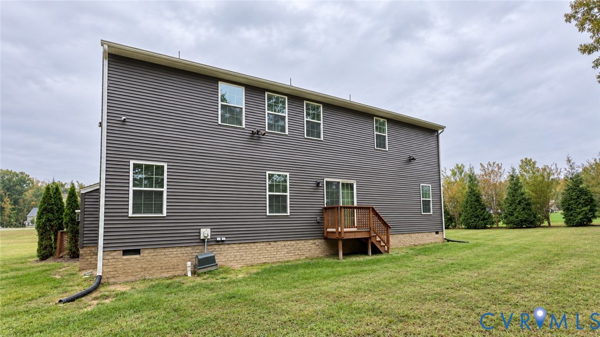 Dark horizontal siding exterior featuring a brick foundation, wood-framed rear deck, sliding glass door, and expansive lawn