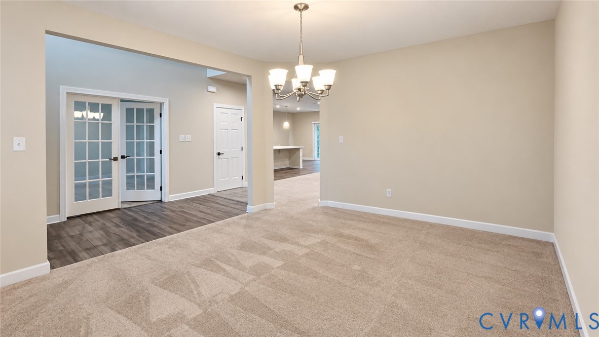 Neutral-toned carpeting, wood-finish flooring, multi-pane French doors, and a decorative five-light chandelier Neutral-toned carpeting, wood-finish flooring, multi-pane French doors, and a decorative five-light chandelier