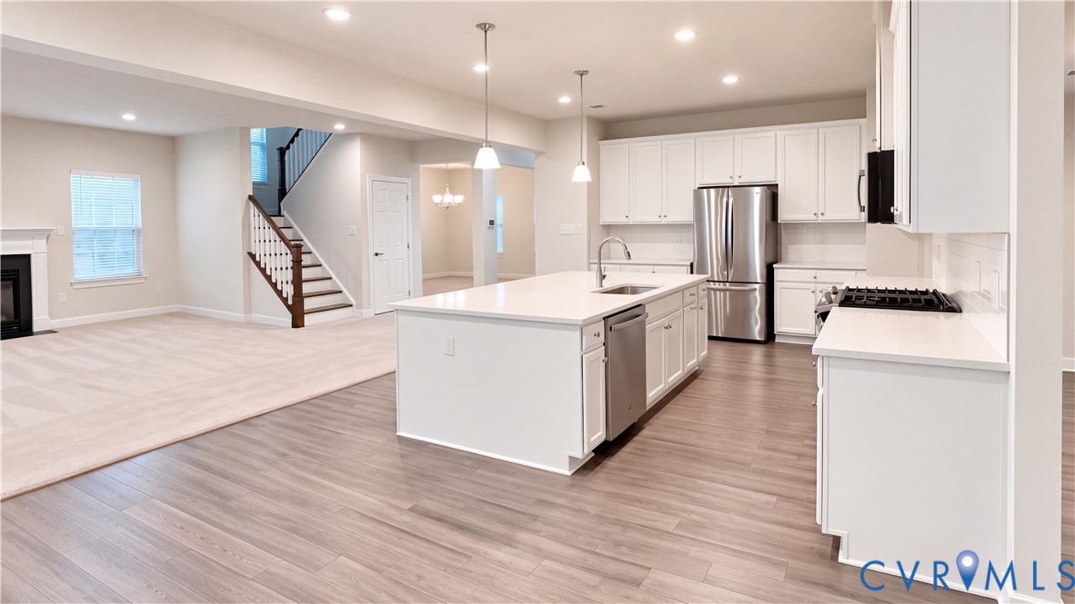 Kitchen featuring white cabinetry, an expansive center island with stone-finish countertops, stainless steel appliances, pendant lighting, and wood-finish flooring Kitchen featuring white cabinetry, an expansive center island with stone-finish countertops, stainless steel appliances, pendant lighting, and wood-finish flooring