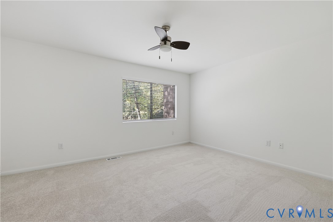 Neutral interior room featuring neutral carpeting, a central ceiling fan with integrated lighting, and a window with horizontal blinds
