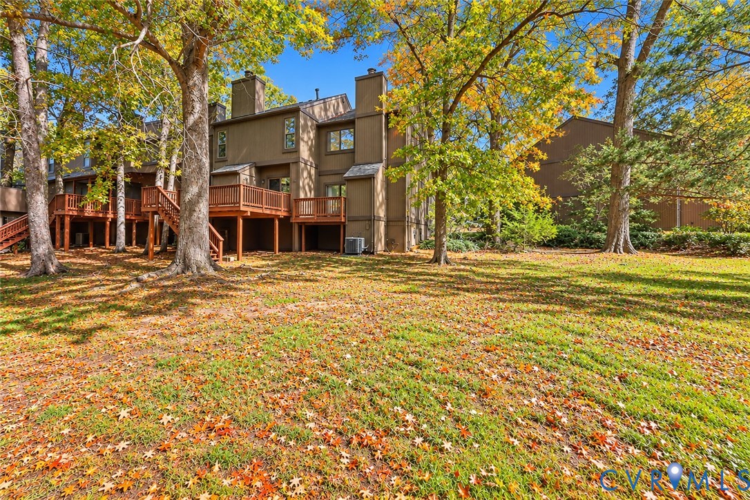 Multi-story exterior featuring wood siding, elevated wood decking, brick chimneys, and mature trees across the surrounding landscape