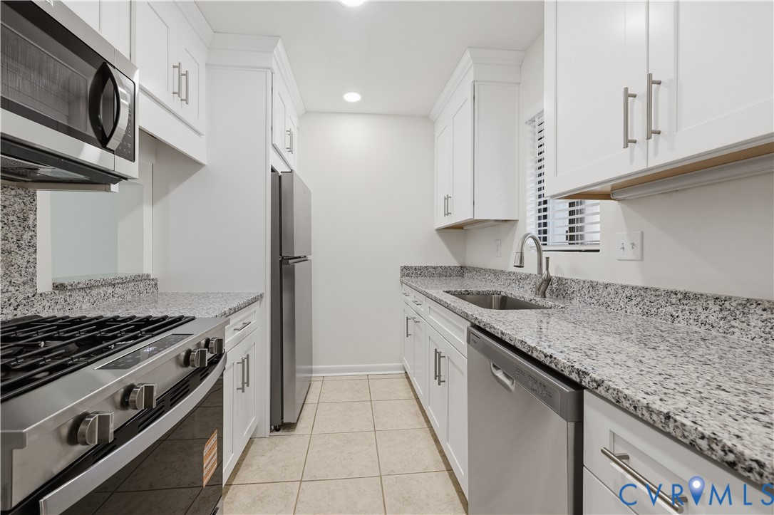 Kitchen featuring white cabinetry, stone-surface countertops, tile flooring, stainless steel appliances, and a gooseneck faucet
