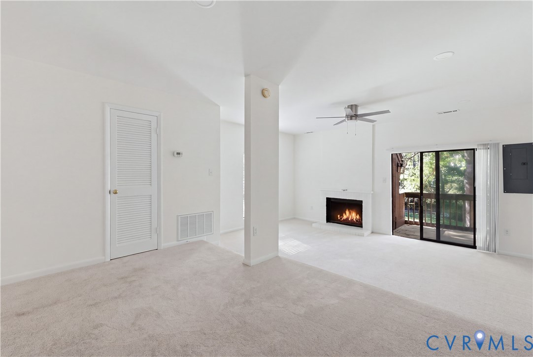 Neutral-toned wall-to-wall carpeting, fireplace with a white mantel, sliding glass doors, and a ceiling fan