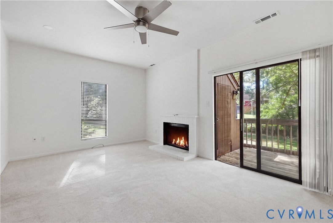 Living space featuring a white fireplace with a raised hearth, sliding glass doors, neutral carpeting, and a ceiling fan