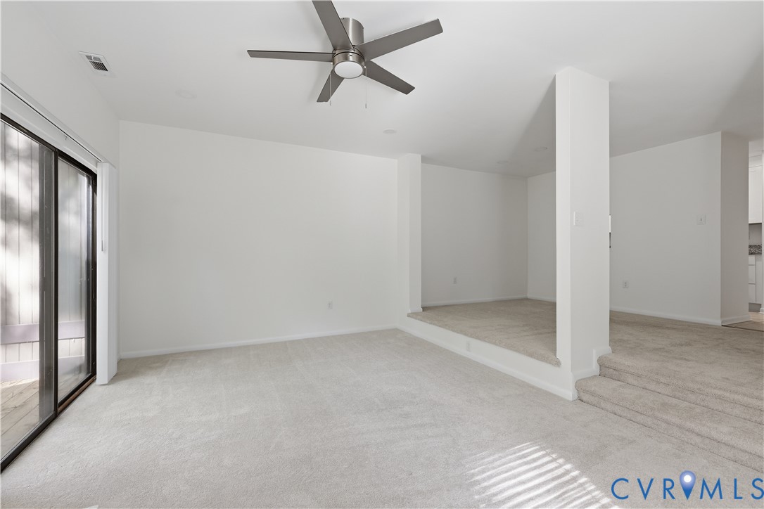 Multi-level floor plan featuring carpeted flooring, a recessed platform area, structural pillars, a ceiling fan with integrated lighting, and sliding glass doors
