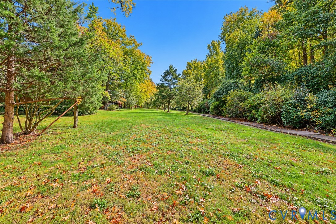 Expansive backyard featuring a sprawling lawn, mature trees, and a paved stone pathway
