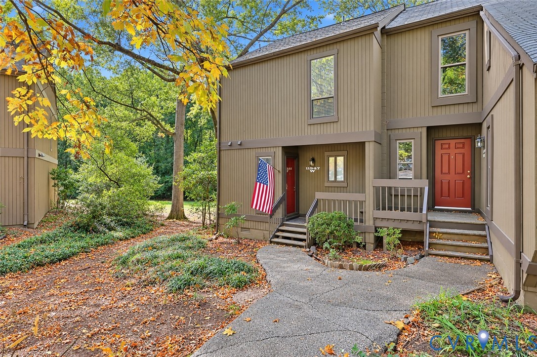 Multi-level exterior featuring vertical wood siding, a red front door, covered wood porch, and a paved walkway Multi-level exterior featuring vertical wood siding, a red front door, covered wood porch, and a paved walkway