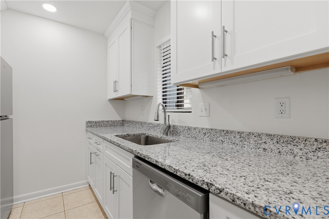 Kitchen featuring white shaker-style cabinetry, speckled stone countertops, a stainless steel undermount sink with a gooseneck faucet, stainless steel dishwasher, and tile flooring