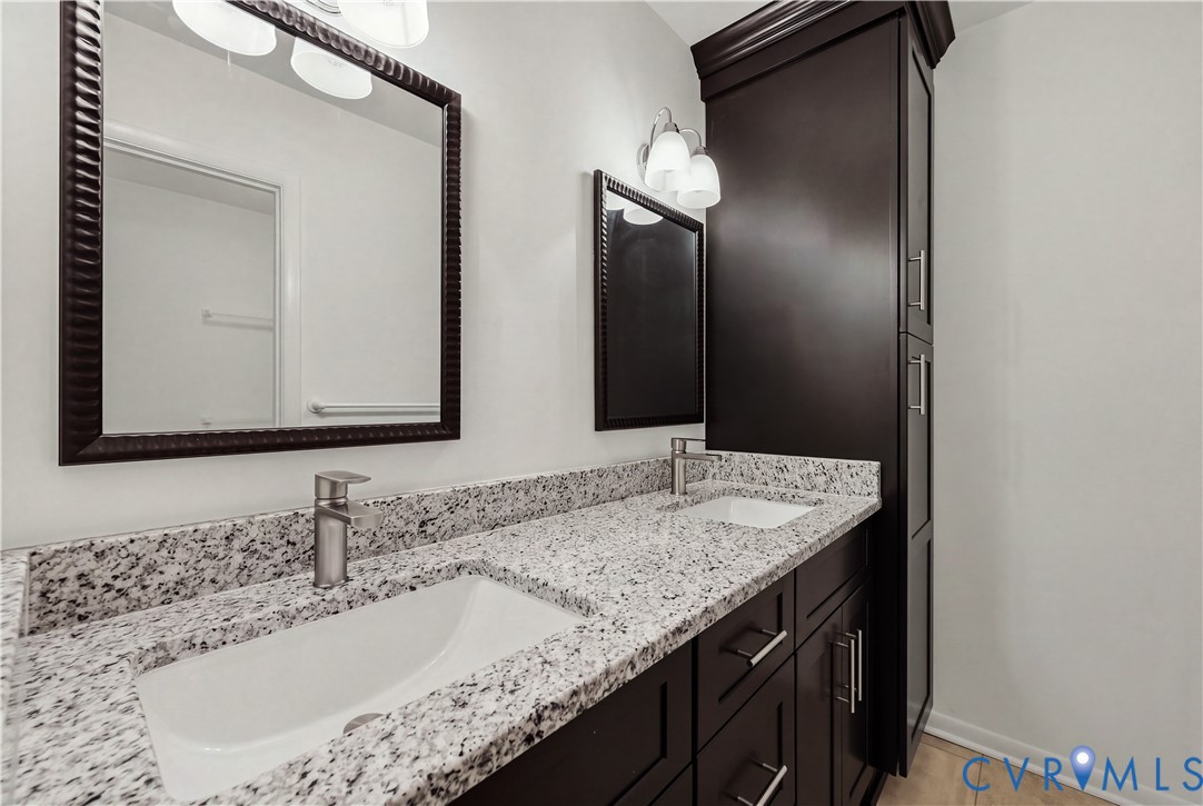 Double vanity featuring dark wood-finish cabinetry, a stone-composite countertop, dual undermount sinks, and integrated floor-to-ceiling storage cabinetry