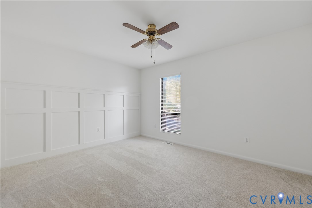 Neutral wall tones, wall wainscoting, wall-to-wall carpeting, and a central ceiling fan with integrated light fixture