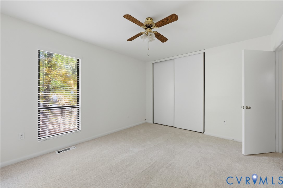 Neutral wall finishes, carpeting, ceiling fan with light fixture, sliding door closet, and window with blinds