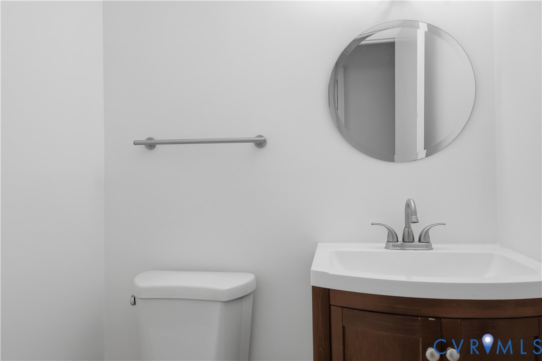 Bathroom featuring a wood-finish vanity with a white integrated basin, a polished metal faucet, a circular wall-mounted mirror, and a metal towel bar