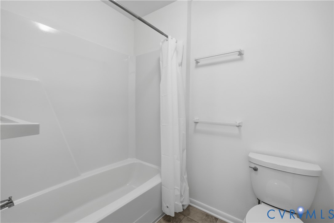 Full bathroom featuring a tub-shower combination with integrated wall surround, dual chrome wall-mounted towel bars, and a white porcelain toilet
