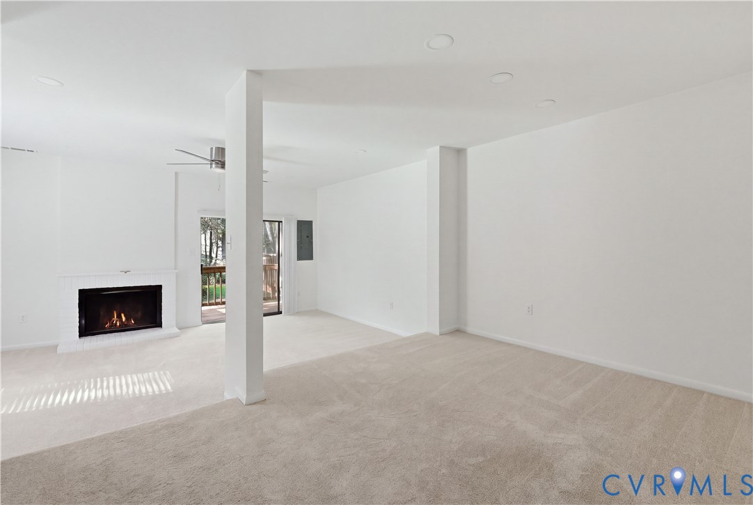 Neutral-toned carpeted flooring, fireplace with a painted masonry surround, recessed lighting, and sliding glass door leading to an outdoor deck