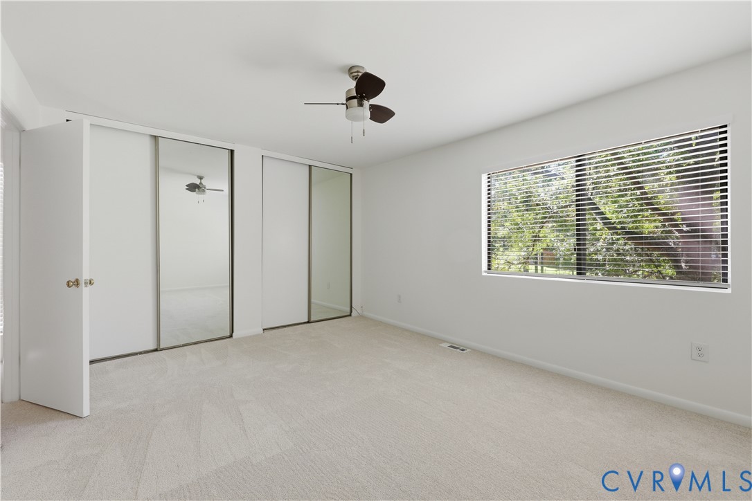 Neutral-toned carpeting, dual sliding mirror-paneled closet doors, and ceiling-mounted fan with integrated light fixture
