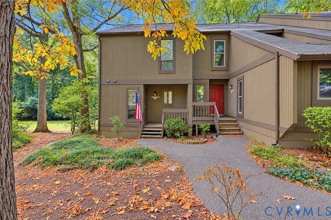 Vertical wood siding exterior featuring a paved walkway, raised wood-frame deck, and mature surrounding landscape