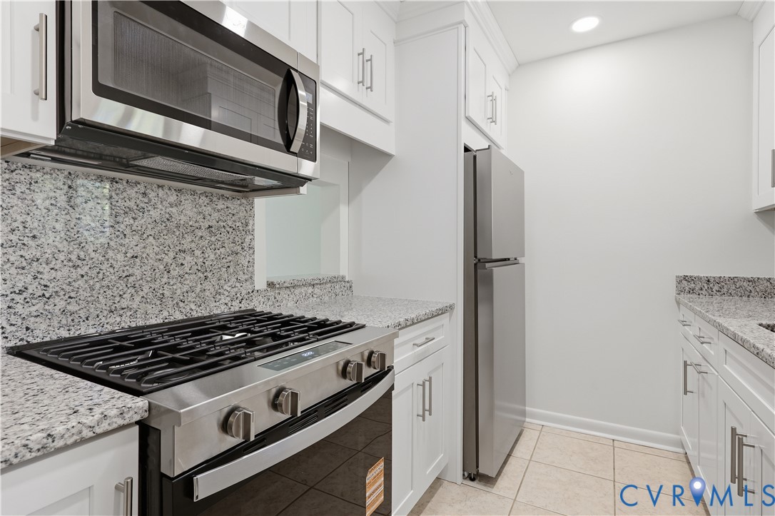 Kitchen featuring white cabinetry with metallic hardware, stone-finish countertops, tile flooring, and stainless steel appliances including a gas range and built-in microwave