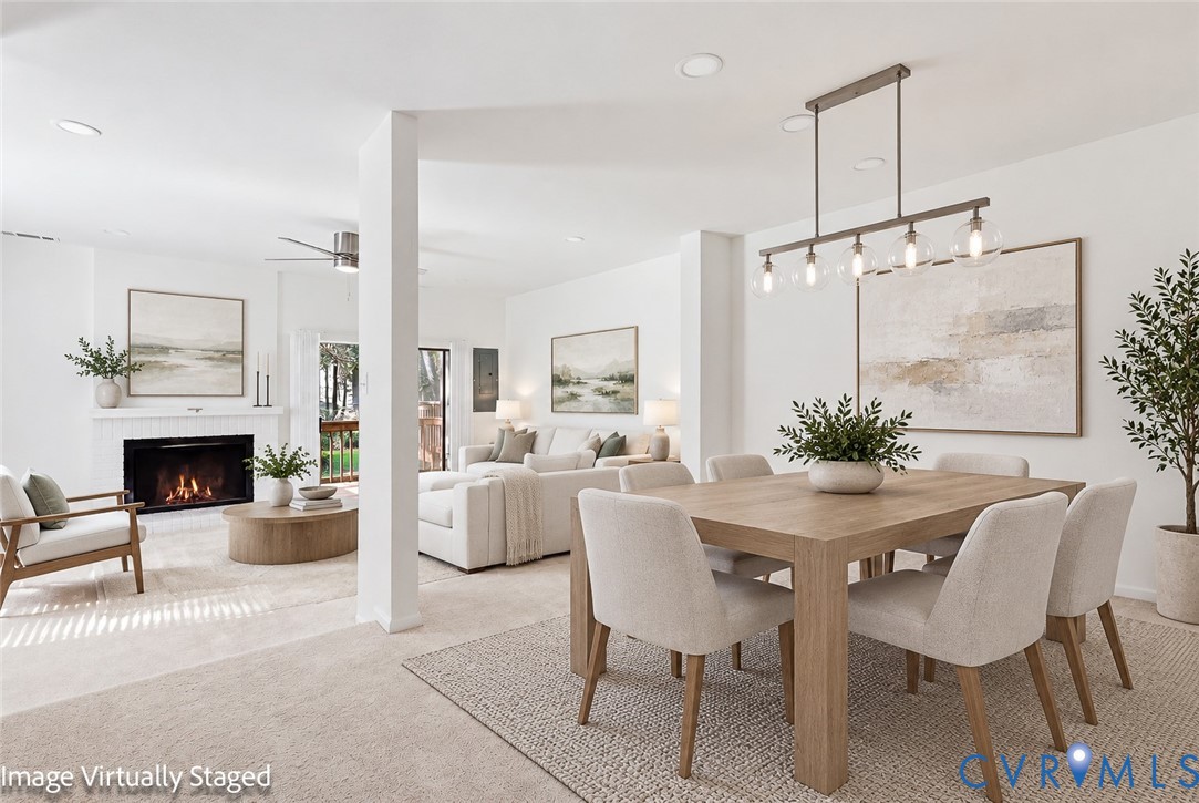 Open-concept interior featuring a wood-burning fireplace with a mantel, linear multi-bulb pendant lighting, recessed lighting, and carpeted flooring