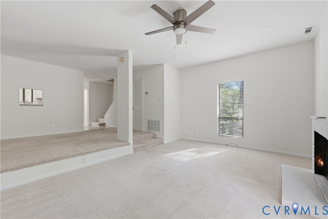 Multi-level living area featuring neutral carpeting, a built-in white fireplace, recessed ceiling lighting, and a modern metal ceiling fan