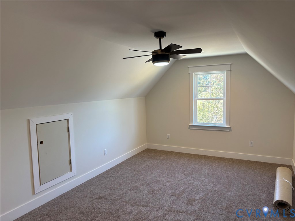 Interior room featuring vaulted ceilings, neutral-toned carpeting, a single-hung window with casing, and a multi-blade ceiling fan with an integrated light fixture