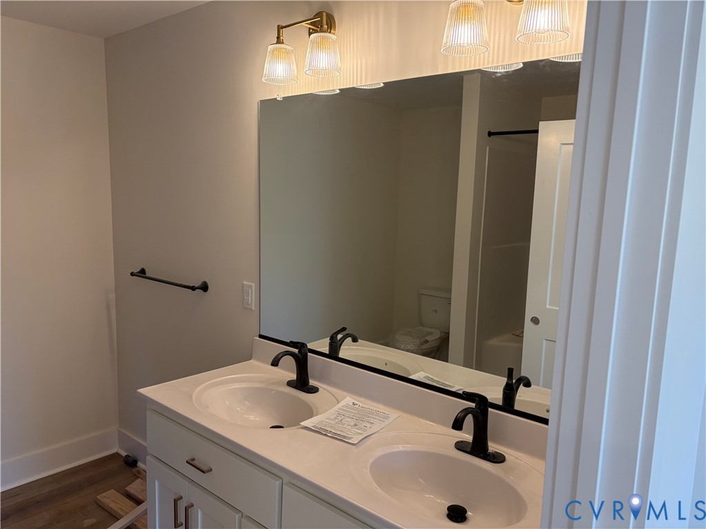 Double vanity featuring white cabinetry, integrated sinks, dark metal fixtures, and an expansive wall-mounted mirror accented by multi-bulb vanity lighting