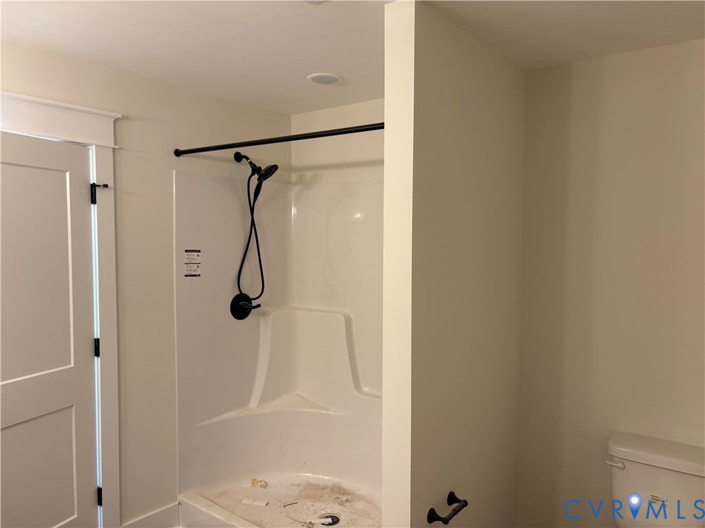 Shower enclosure with a white acrylic surround, handheld showerhead, matte black hardware, and recessed ceiling lighting