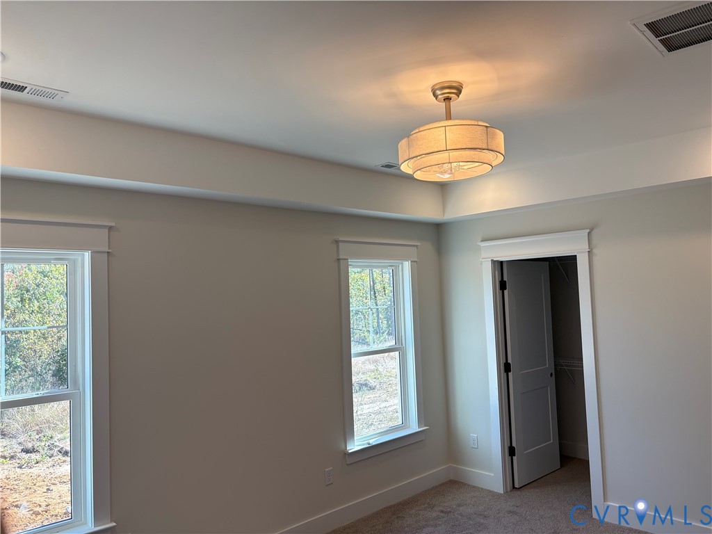 Tray ceiling with a multi-tiered fabric drum light fixture, windows with heavy casing, and a walk-in closet featuring a paneled door