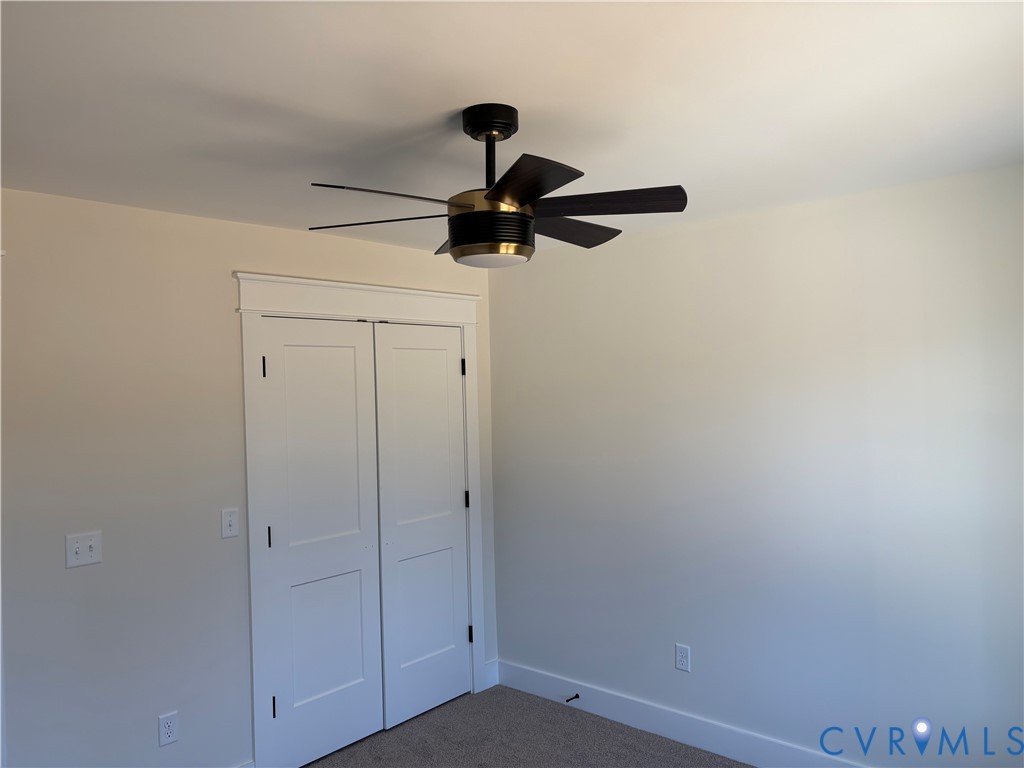 Modern ceiling fan with integrated light fixture and metallic housing, double-panel closet doors featuring decorative header trim, and neutral wall-to-wall carpeting