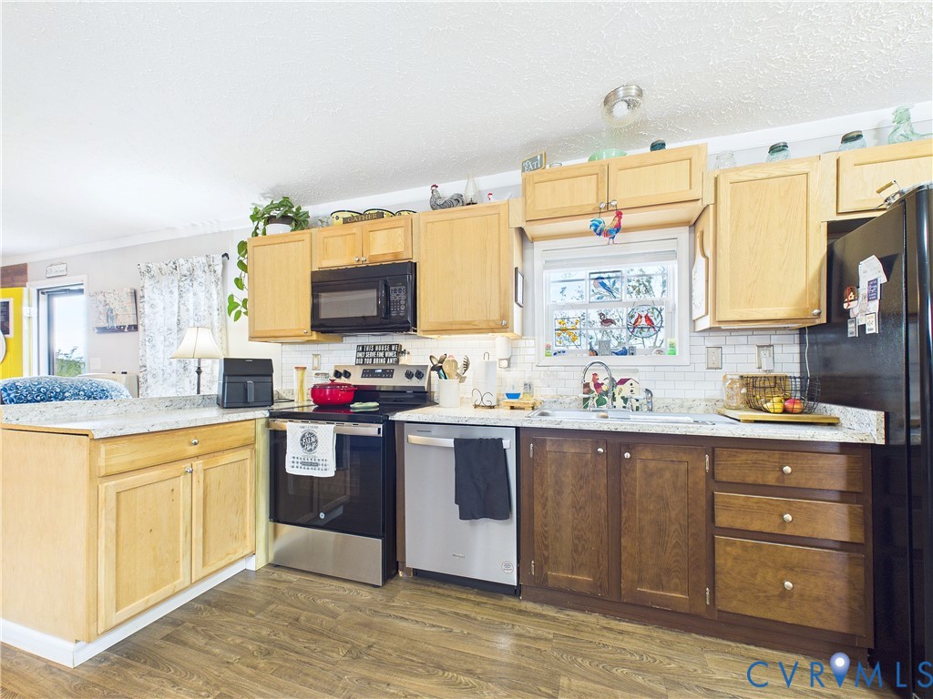 Kitchen featuring wood cabinetry, stone-finish countertops, subway tile backsplash, stainless steel dishwasher, and wood-finish flooring Kitchen featuring wood cabinetry, stone-finish countertops, subway tile backsplash, stainless steel dishwasher, and wood-finish flooring