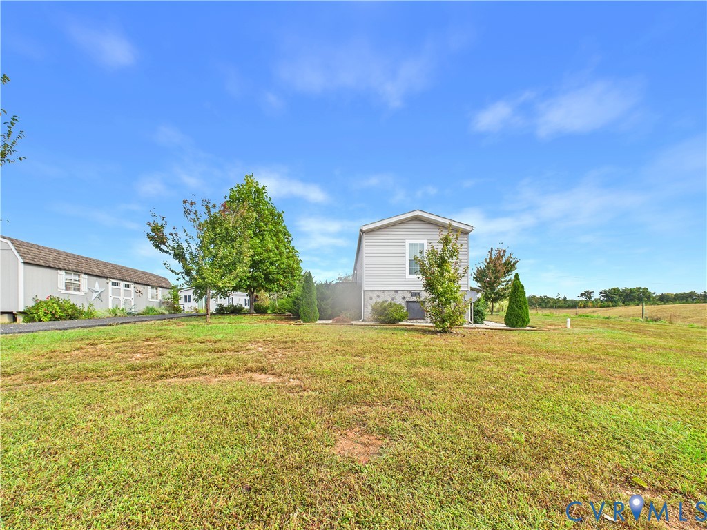 Expansive exterior grounds featuring a manicured lawn, a detached storage building, stone-pattern foundation skirting, and mature landscaping