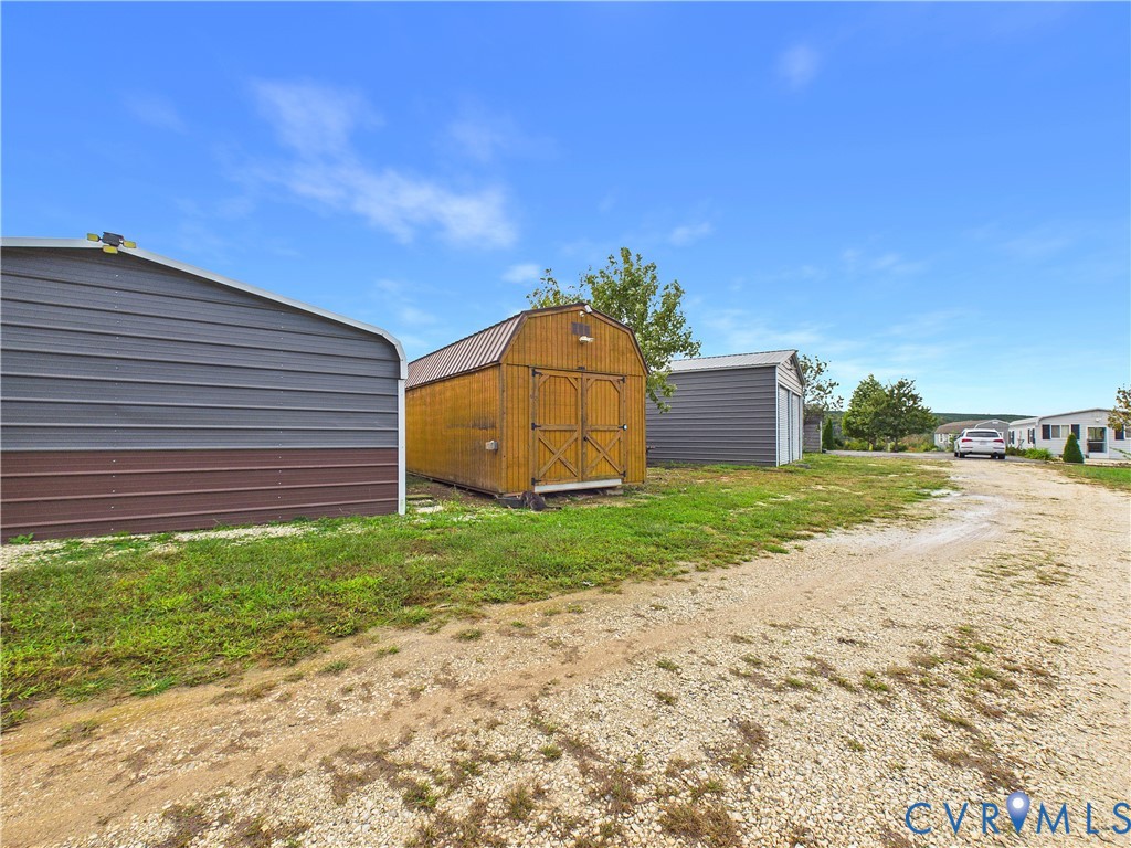 Exterior storage structures featuring two metal-sided buildings and a central wood-sided outbuilding with dual doors, situated on a gravel driveway