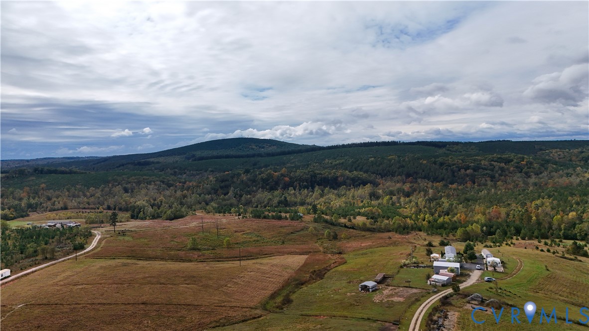 Expansive acreage featuring rolling open fields, scattered mature trees, winding gravel paths, and a prominent mountain backdrop