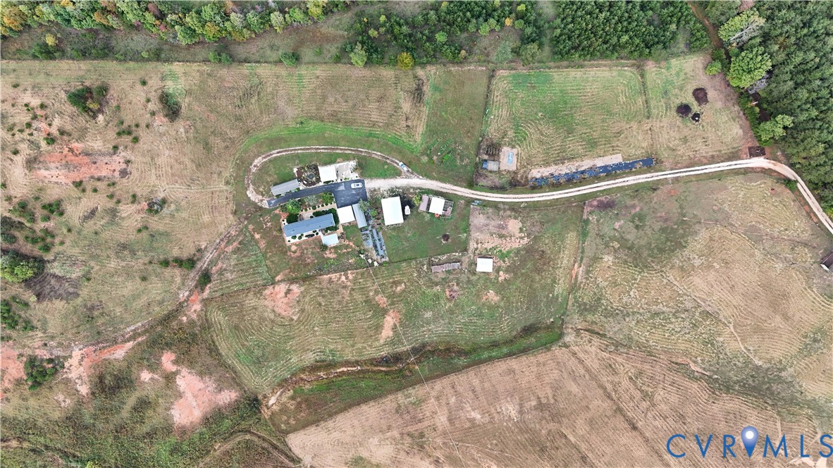 Aerial perspective of a sprawling acreage featuring an expansive open field, multiple detached outbuildings, a private gravel driveway, and dense perimeter tree lines