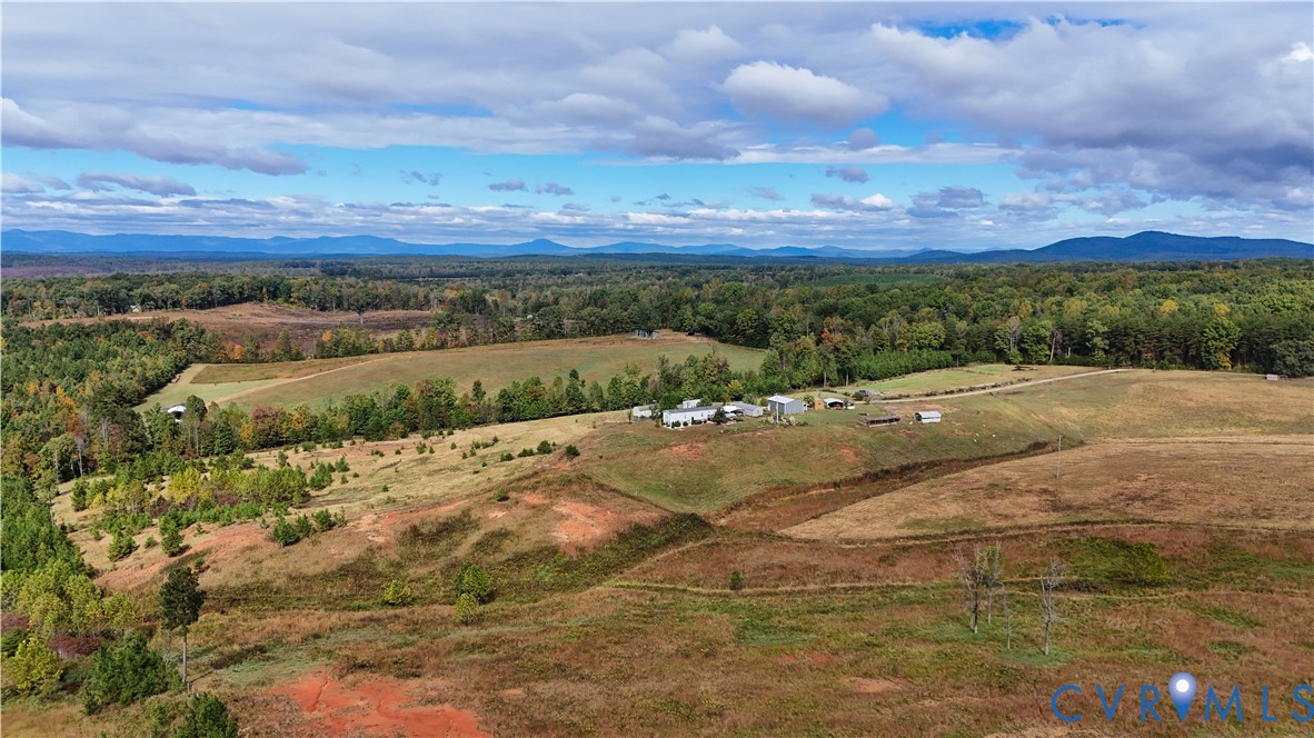 Expansive acreage featuring rolling open fields, mature woodland, multiple outbuildings, and mountain scenery