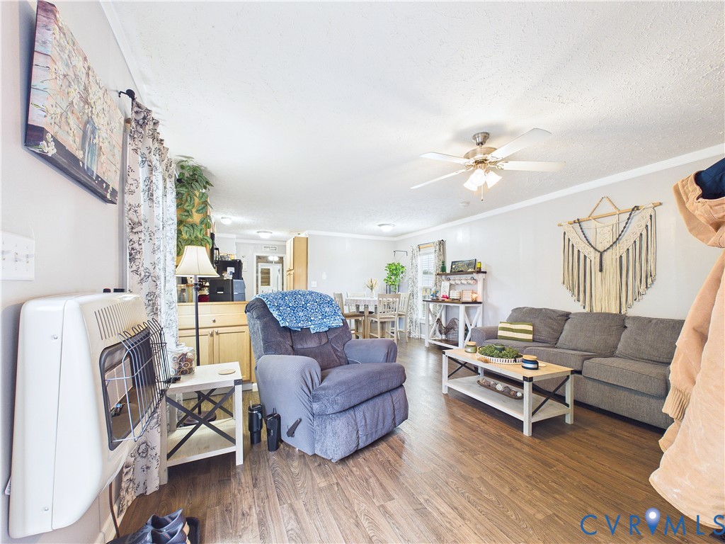 Open-concept interior featuring wood-finish flooring, a white wall-mounted gas heater, and a multi-blade ceiling fan with integrated lighting Open-concept interior featuring wood-finish flooring, a white wall-mounted gas heater, and a multi-blade ceiling fan with integrated lighting