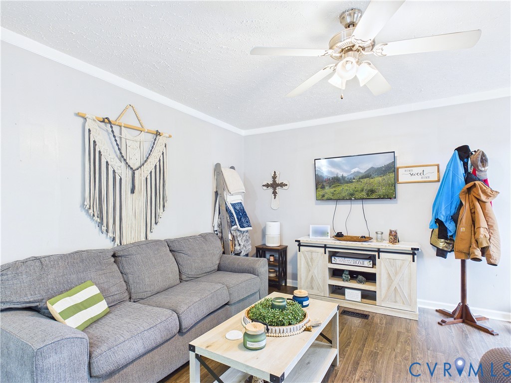 Neutral-toned walls featuring crown molding, wood-finish flooring, and a ceiling-mounted light fixture with integrated fan