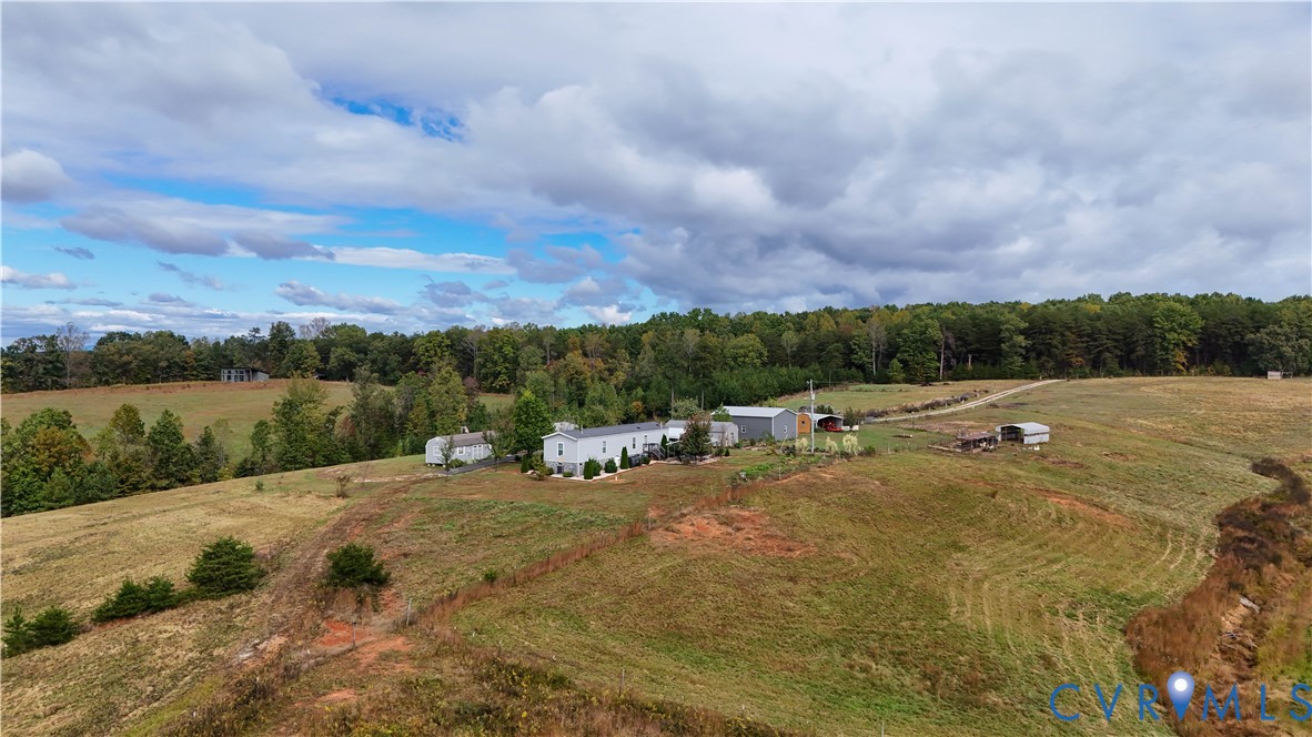 Aerial perspective of expansive acreage featuring open rolling topography, mature tree lines, and multiple detached outbuildings
